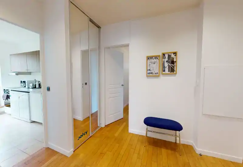 Bright, minimal entrance hallway with wooden flooring, a small upholstered bench and a mirrored built-in closet; connects directly to the kitchen.