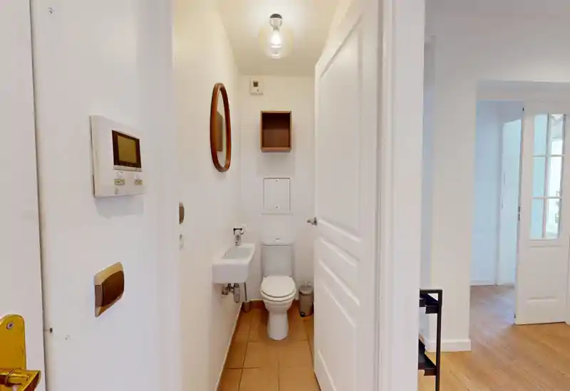 Compact guest bathroom with a wall-mounted sink, toilet and small mirror; bright, clean and simply styled — ideal for a city apartment.