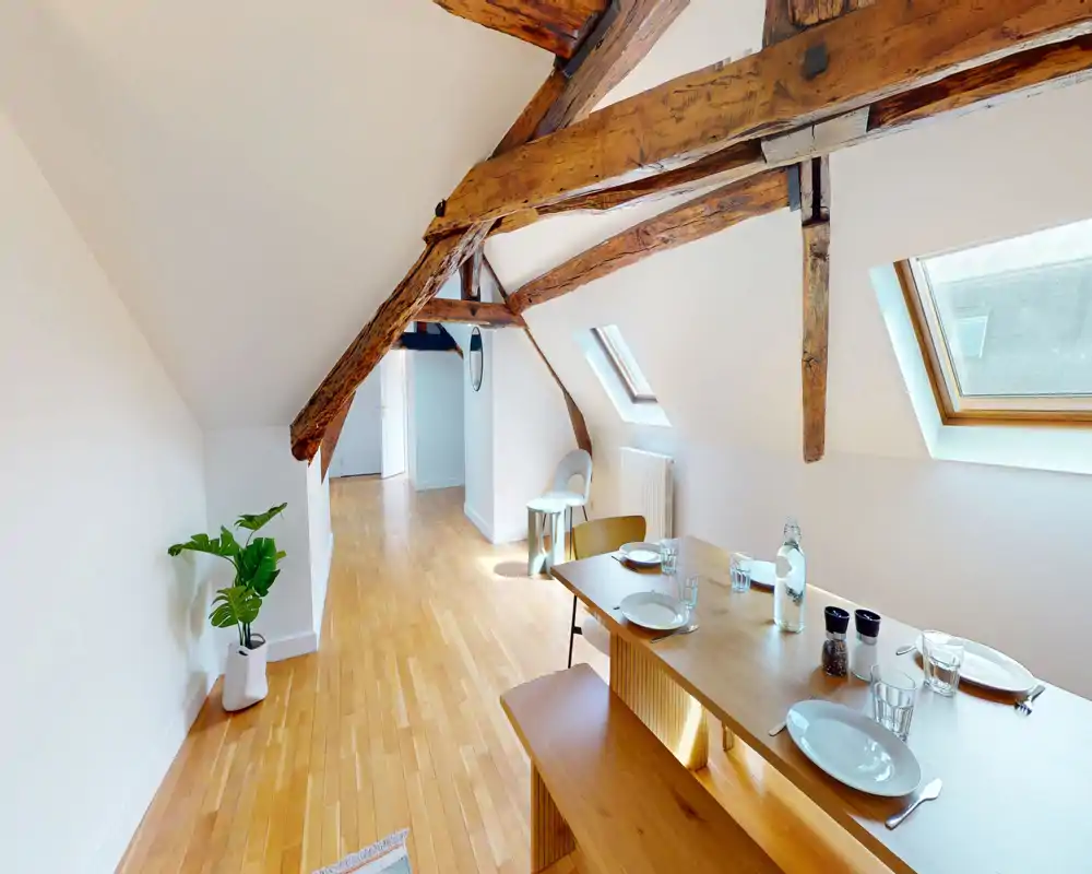 Bright attic dining area with exposed wooden beams, a wooden bench and table set for four beneath skylights — a warm, airy space ideal for casual meals.