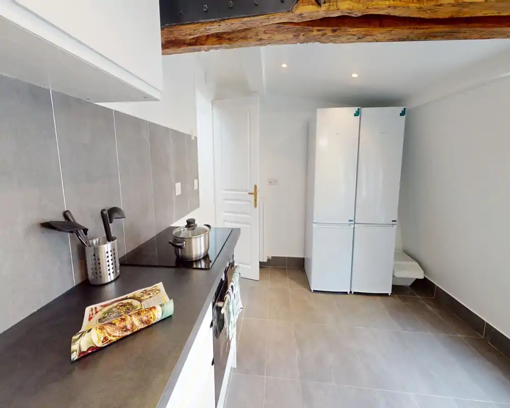 Bright, modern kitchen with tiled floor, induction hob, large double fridge and exposed wooden beam — practical and clean layout ideal for a rental.