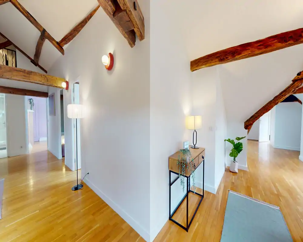 Bright, airy entrance/hallway with exposed wooden beams, polished hardwood floors and minimal decorative console table; a welcoming transitional space connecting rooms.