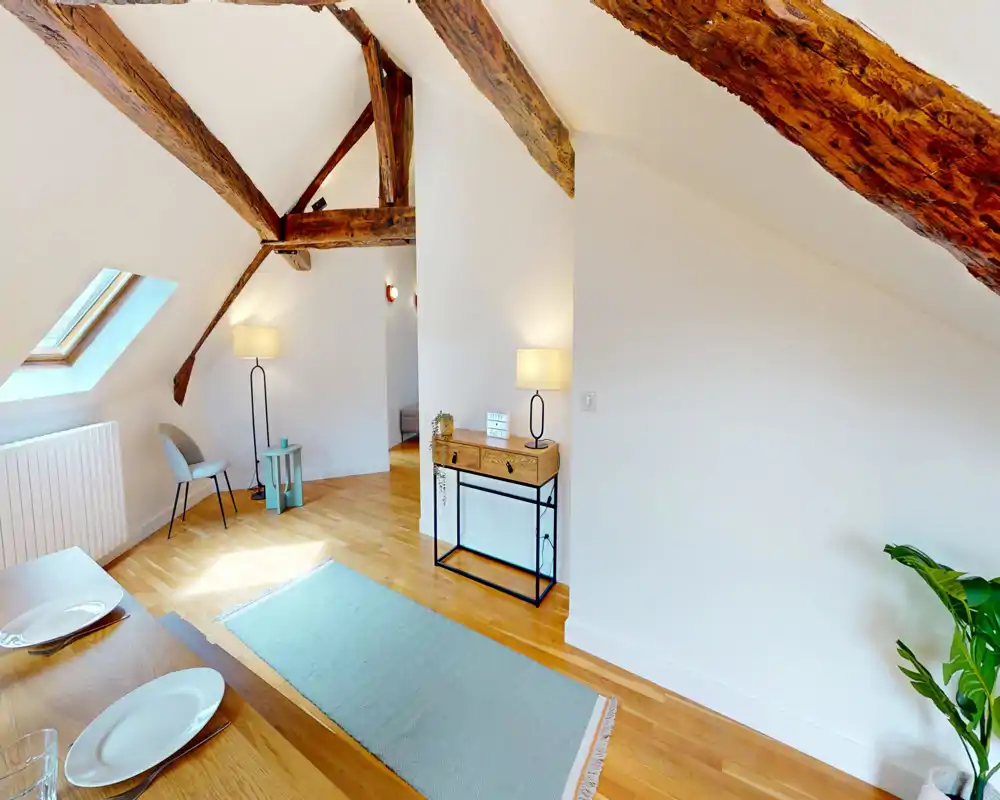 Bright, airy living area under a pitched roof with exposed wooden beams, a skylight, a cozy rug and stylish lamps — ideal for a comfortable attic-style lounge.