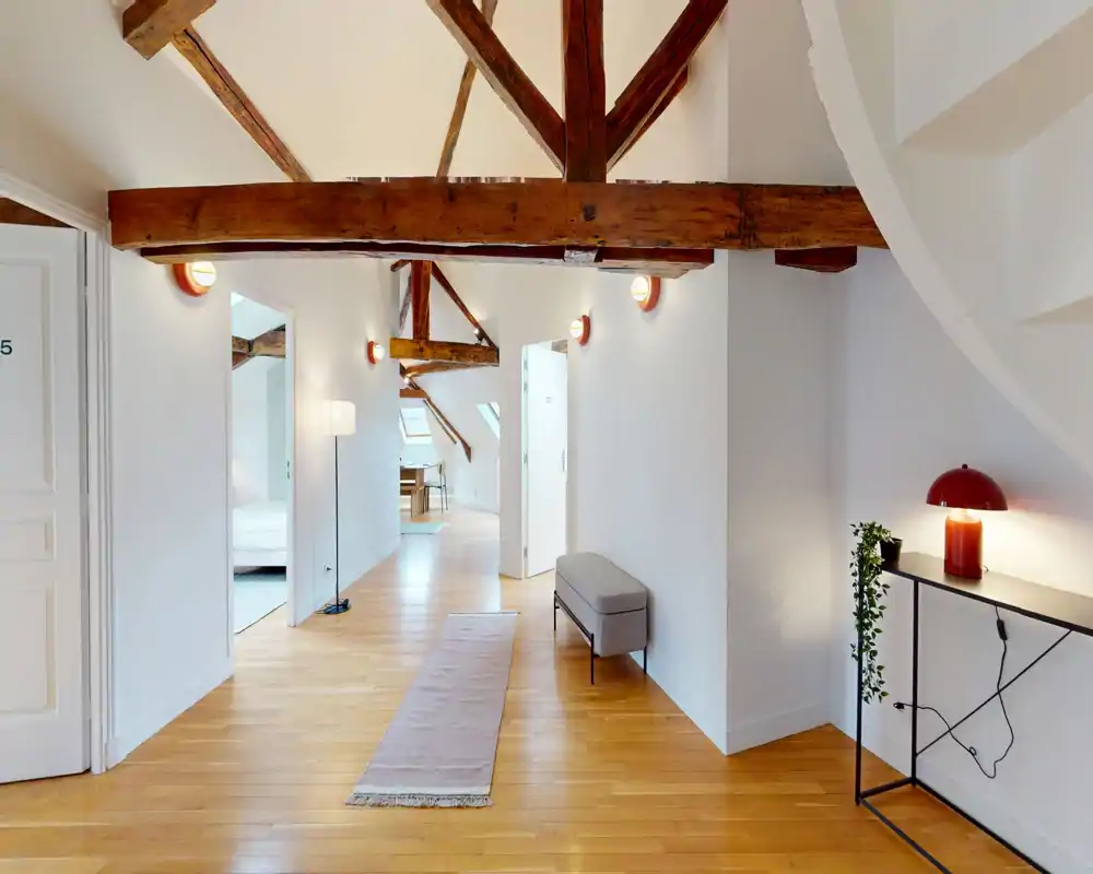 Bright, airy hallway / living area with exposed wooden beams, a long runner rug, bench seating and a modern console lamp — an elegant transitional space connecting rooms.