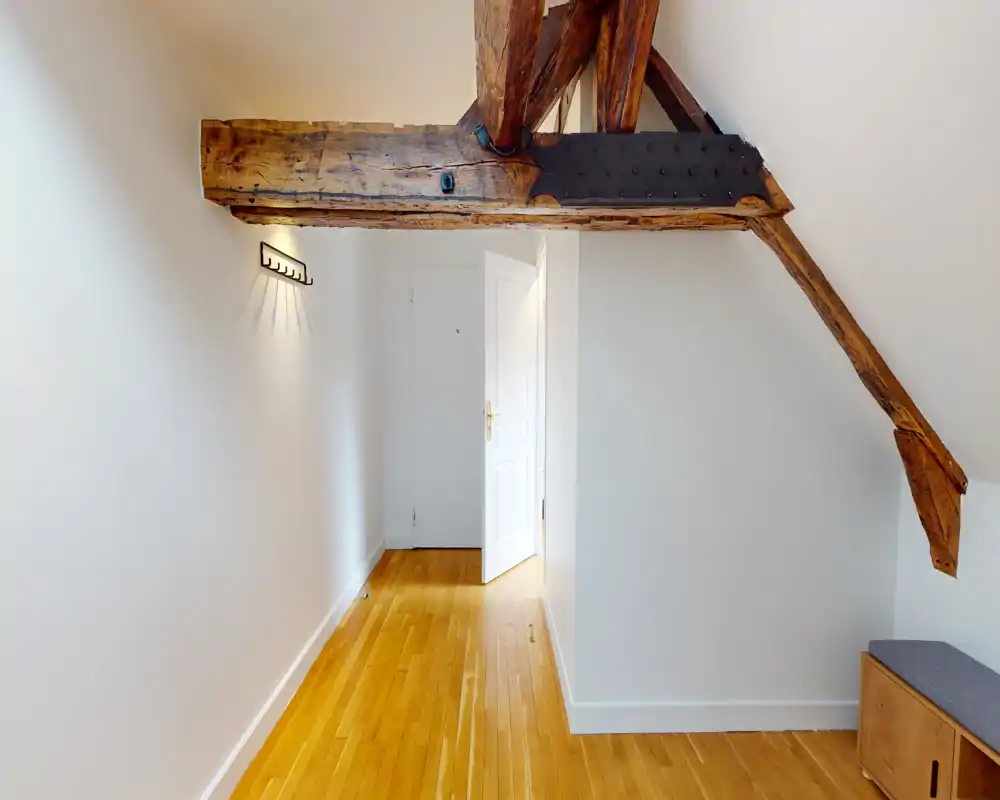 Bright, narrow entrance/hallway with polished wooden floor, exposed wooden beams and a white door at the end — ideal as an inviting entry space.
