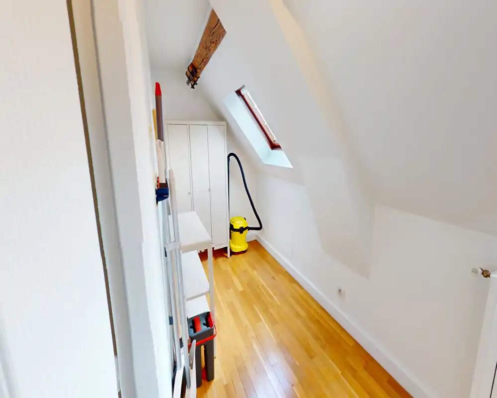 Small bright attic entrance / storage area with sloped ceiling, wooden floor, built-in wardrobe and cleaning equipment.