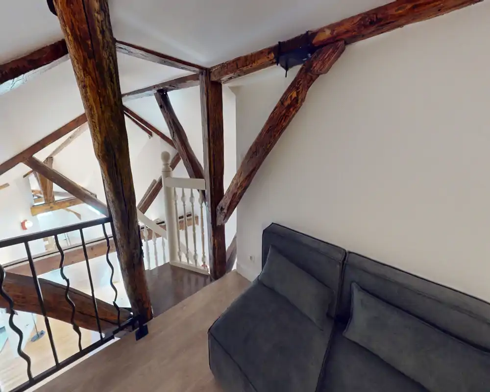A cozy loft corner with exposed wooden beams and a compact sofa overlooking the lower level; bright, airy atmosphere ideal for relaxing.
