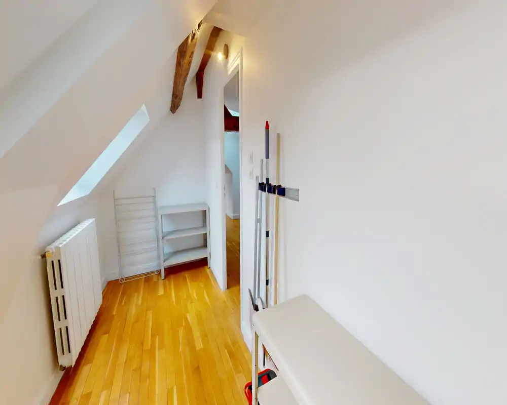 Narrow bright entrance or small corridor with sloped ceiling, wooden floor, radiator and storage shelving — a tidy transitional space connecting rooms.