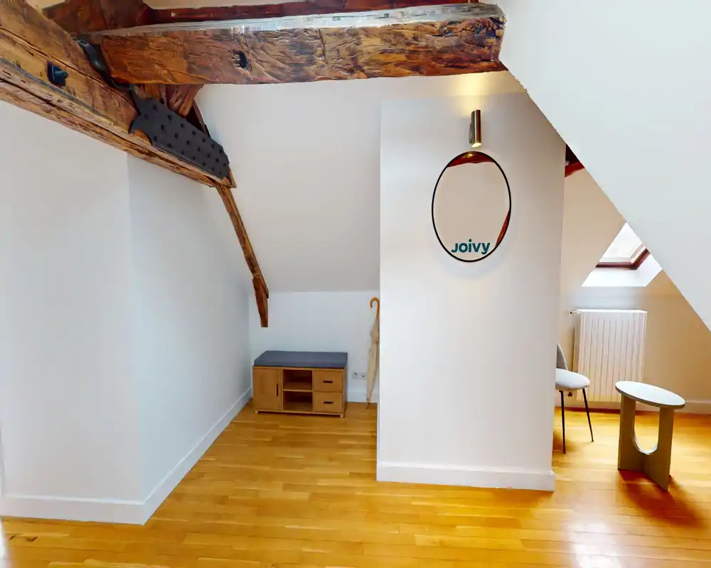 Bright attic entrance or landing with exposed wooden beams, parquet flooring, a small bench with storage and a skylight — a welcoming transition area.