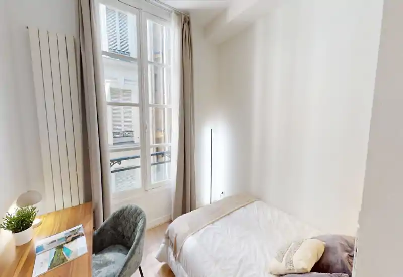 Camera da letto luminosa e compatta con letto comodo, ampia finestra che illumina la stanza, una scrivania e una poltrona accogliente — ideale per una persona o una coppia.