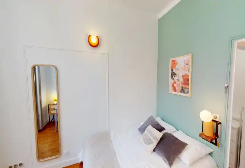 Camera da letto luminosa e di stile con un comodo letto matrimoniale, cuscini decorativi, lampada da comodino e una parete verde salvia che dona carattere.