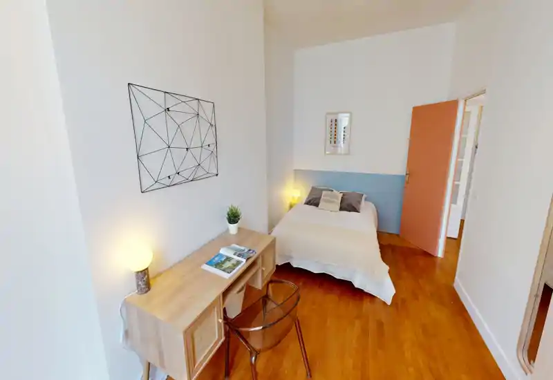 Camera da letto accogliente e luminosa con letto matrimoniale, lampade da comodino e una piccola scrivania. Pavimento in legno caldo e tessuti morbidi donano un’atmosfera piacevole.