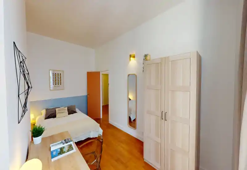 Camera da letto luminosa e ben arredata con letto matrimoniale, scrivania, armadio e specchio a figura intera. Pavimento in legno e tessili morbidi creano un'atmosfera accogliente, ideale per affitti brevi.