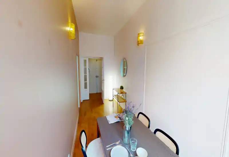 Bright narrow dining area with a wooden table set for two, decorative vase and warm parquet flooring — ideal for compact apartment listings.