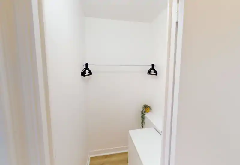Small walk-in closet / entrance alcove with a single hanging rail and drawer unit; clean, minimal and well-lit space suitable for coats or storage.