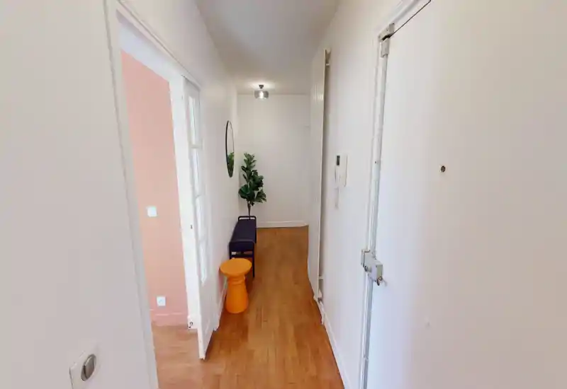 Bright narrow entrance hallway with wooden floor, a small bench, decorative plant and mirror — tidy and welcoming first impression.