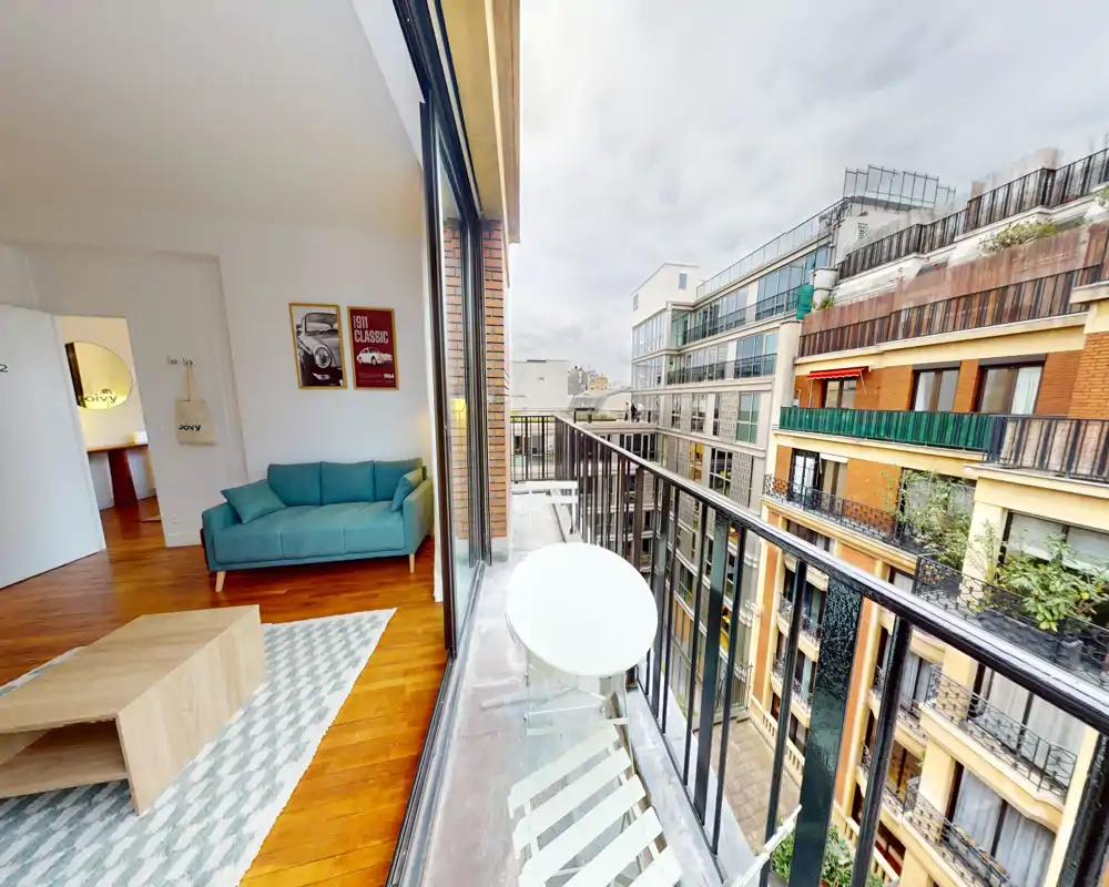 Bright, modern living area with a comfortable teal sofa, wooden floors and a large sliding glass door that opens onto a narrow balcony with city views.