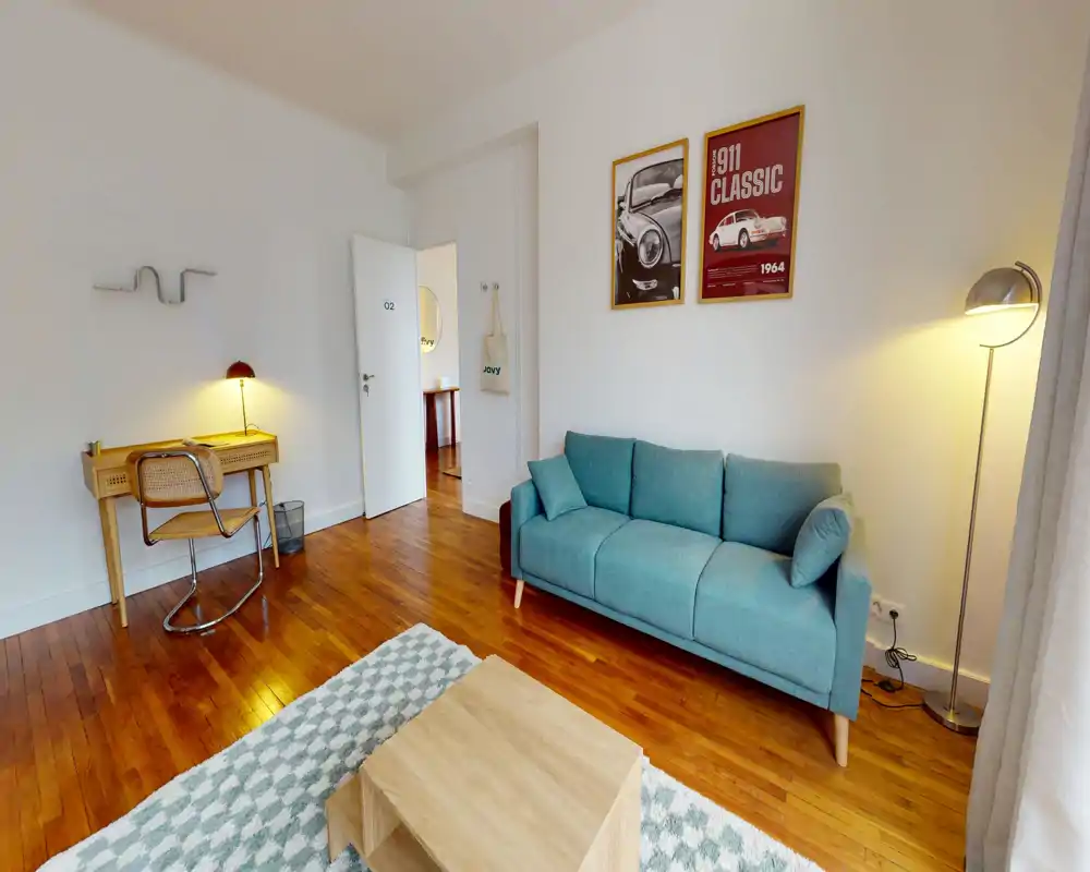 Bright, stylish living room with a teal sofa, wooden floors, a patterned rug and a small wooden coffee table; desk area and warm lamps complete the inviting layout.