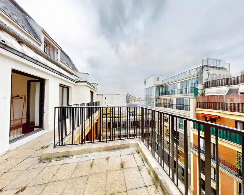 Terrasse privée avec garde-corps en métal donnant sur les immeubles voisins — idéale pour le café du matin ou pour installer du mobilier extérieur ; vue urbaine et accès depuis l'intérieur.