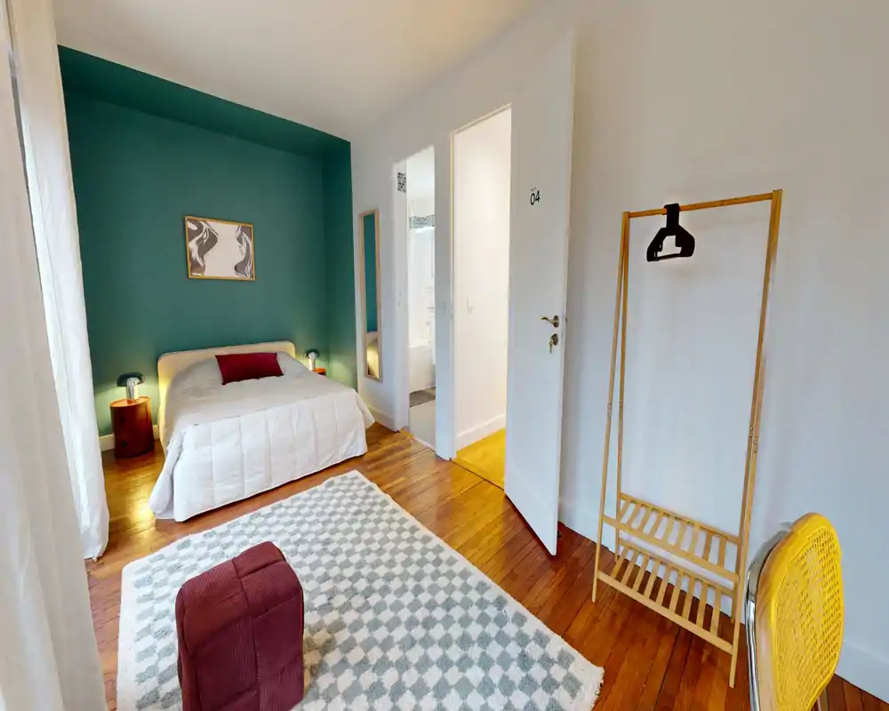 Chambre lumineuse et bien décorée avec un lit double confortable devant un mur d'accent turquoise, lampes de chevet, tapis à motifs et sol en bois — parfaite pour un séjour chaleureux.