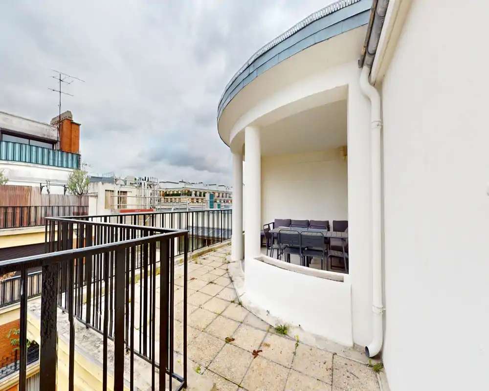 Balcon urbain avec élément architectural arrondi et coin repas extérieur ; vues sur la ville et garde-corps offrant intimité et caractère.