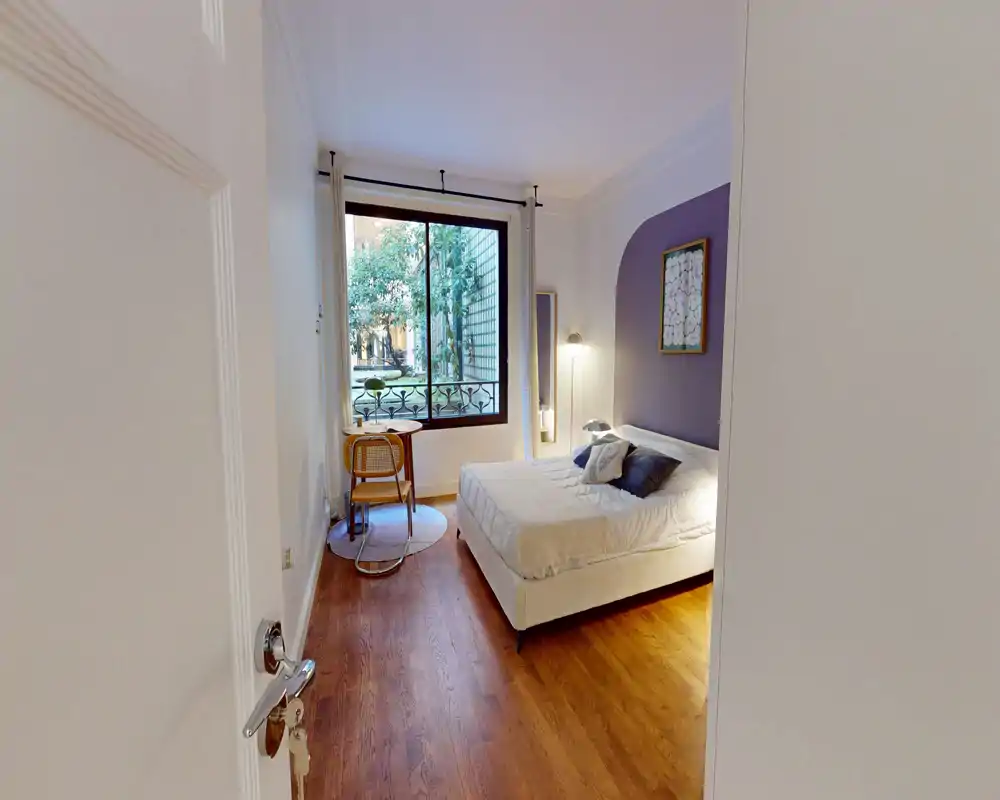 Chambre lumineuse et bien aménagée avec un lit double confortable, une lampe de chevet et une grande fenêtre donnant sur la verdure.