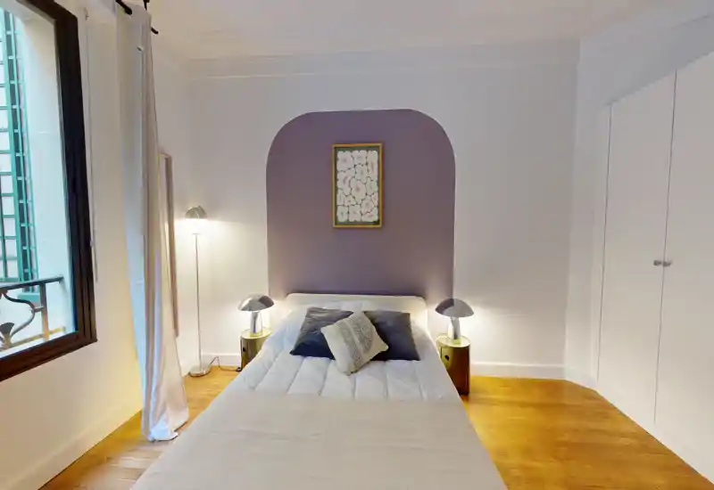 Chambre lumineuse et élégante avec lit double centré, lampes de chevet, coussins décoratifs et une alcôve peinte formant un point focal chaleureux.