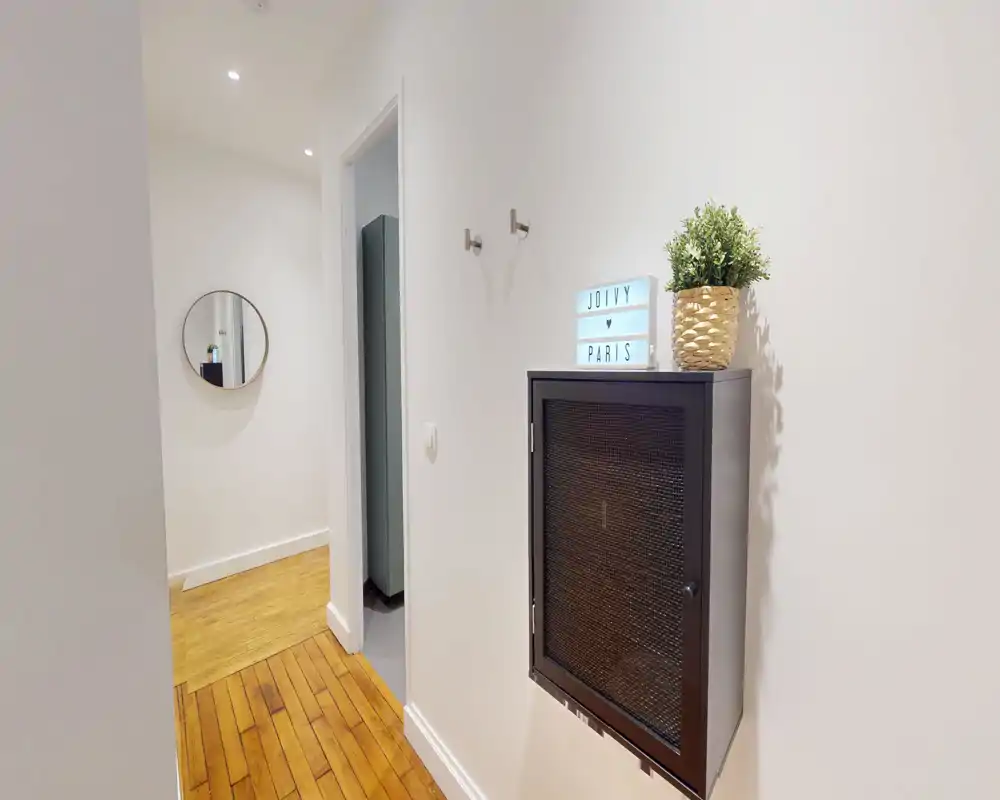 Entrée lumineuse et minimaliste avec sol en bois, meuble mural, petite plante et un miroir rond en arrière-plan.