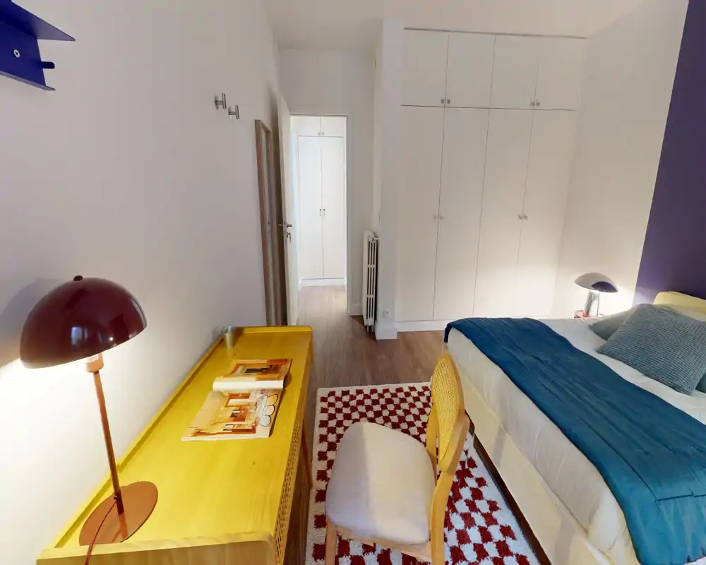 Chambre lumineuse et bien décorée avec grand lit en linge bleu, grands placards intégrés et bureau en bois avec chaise — idéale pour un séjour confortable.
