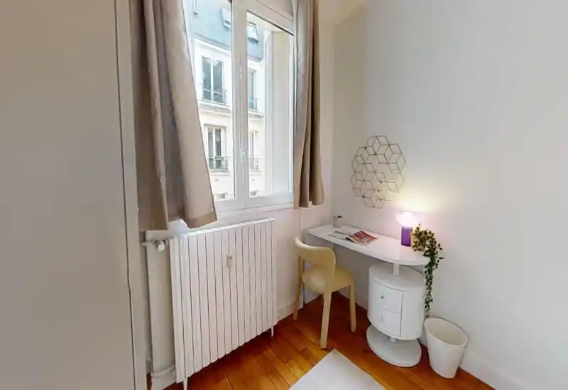 Coin compact avec un petit bureau et une chaise près de la fenêtre, idéal pour un espace de travail individuel ; murs blancs et parquet en bois pour une ambiance lumineuse et minimaliste.