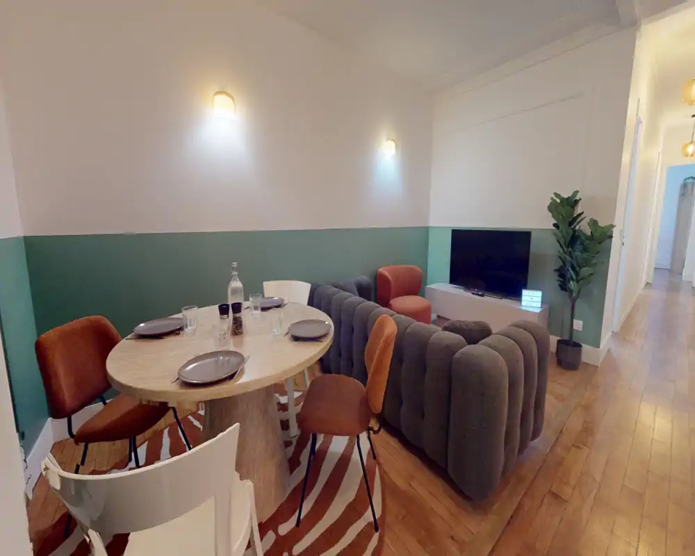 Espace de vie élégant avec canapé courbe, TV et table à manger ronde — parquet chaleureux et murs aux accents verts pour une ambiance cosy et moderne.