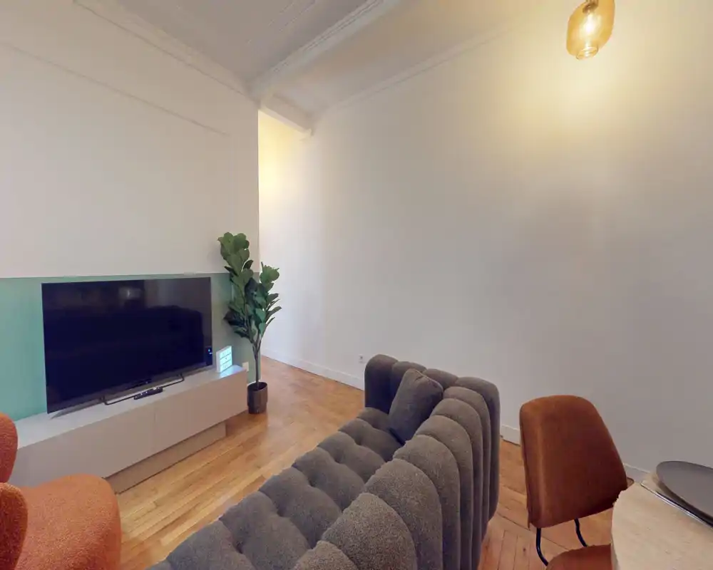 Salon moderne avec canapé gris capitonné, meuble TV et parquet chaleureux — lumineux, élégant et accueillant.