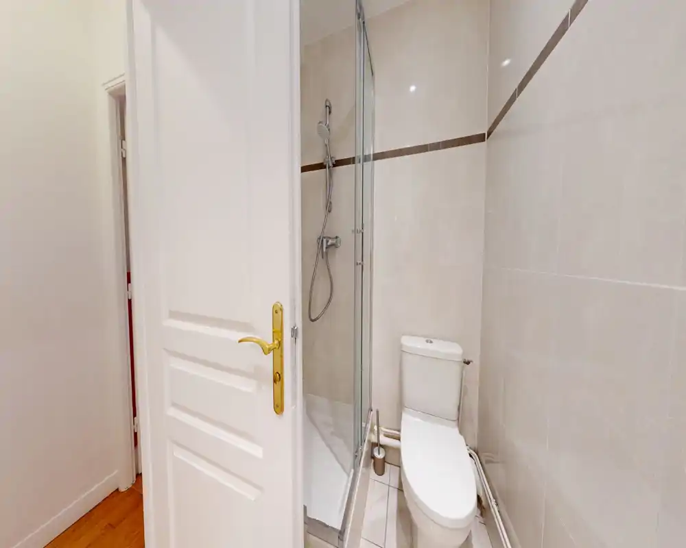 Salle de bains compacte et moderne avec carrelage, une douche d'angle vitrée et des toilettes—lumineuse et propre.