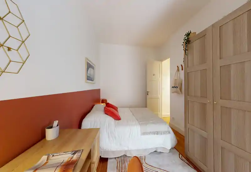 Bright, styled bedroom with a comfortable double bed, warm red accent wall and wooden wardrobe. Soft textiles, a bedside lamp and a rug create a cozy, welcoming atmosphere ideal for rental photos.