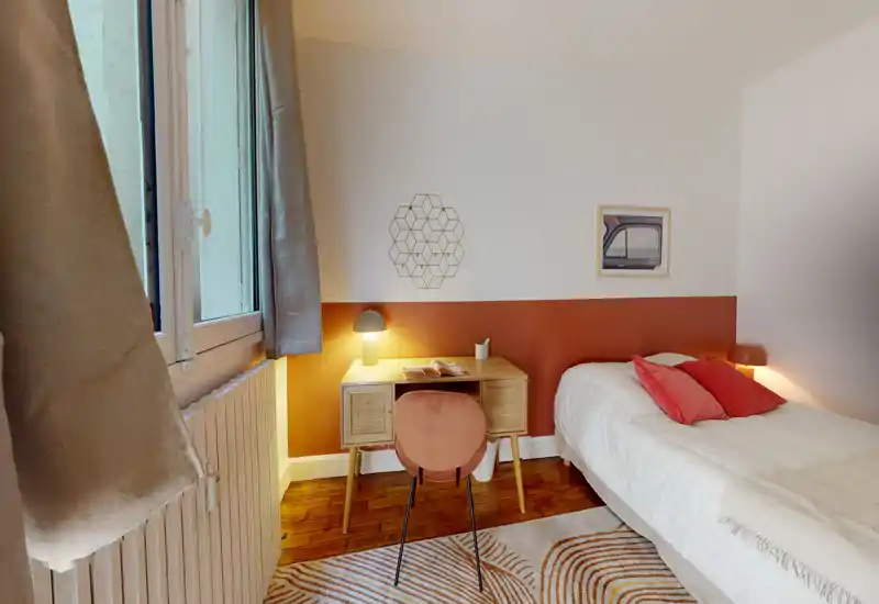 Small, styled bedroom with a single bed, warm accent wall, bedside lamps and a compact desk by the window—bright, cozy and well-lit for a rental listing.