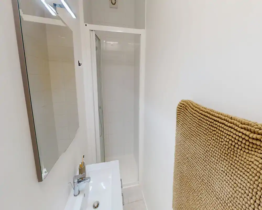 Bagno compatto e luminoso con lavabo, specchio e box doccia piastrellato — pulito e dallo stile semplice, ideale per un piccolo alloggio in affitto.
