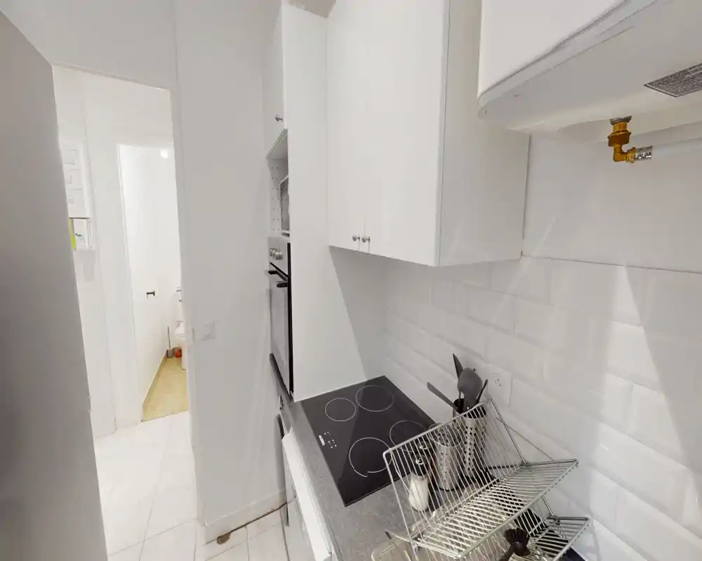 Cucina moderna compatta con mobili bianchi, piano cottura a induzione e paraschizzi piastrellato; disposizione pratica ideale per un appartamento piccolo.