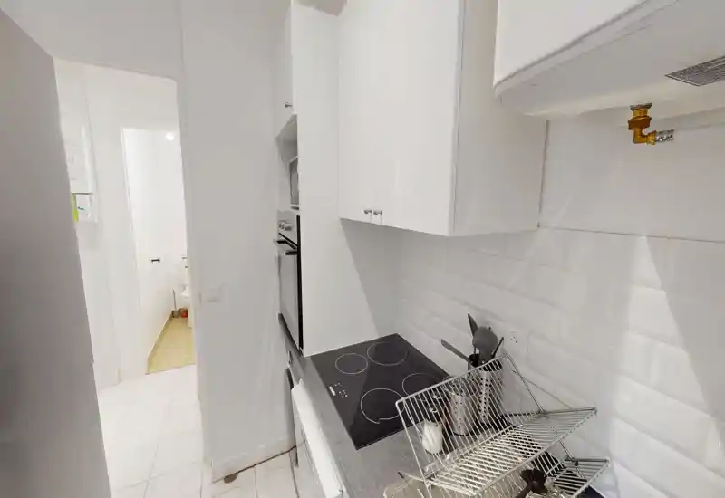 Cuisine moderne et compacte avec placards blancs, plaque à induction et crédence carrelée ; agencement pratique pour un petit appartement.