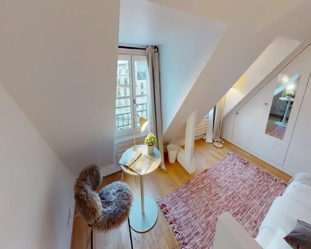 Cozy attic bedroom with angled ceilings, a soft rug and a fur-covered chair by the window. Bright natural light and tasteful decor make this small space welcoming.