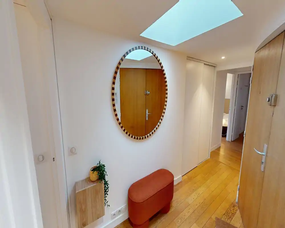 Bright, welcoming entry hall with a decorative round mirror, small bench and wooden flooring — a well-lit space that sets a pleasant first impression.