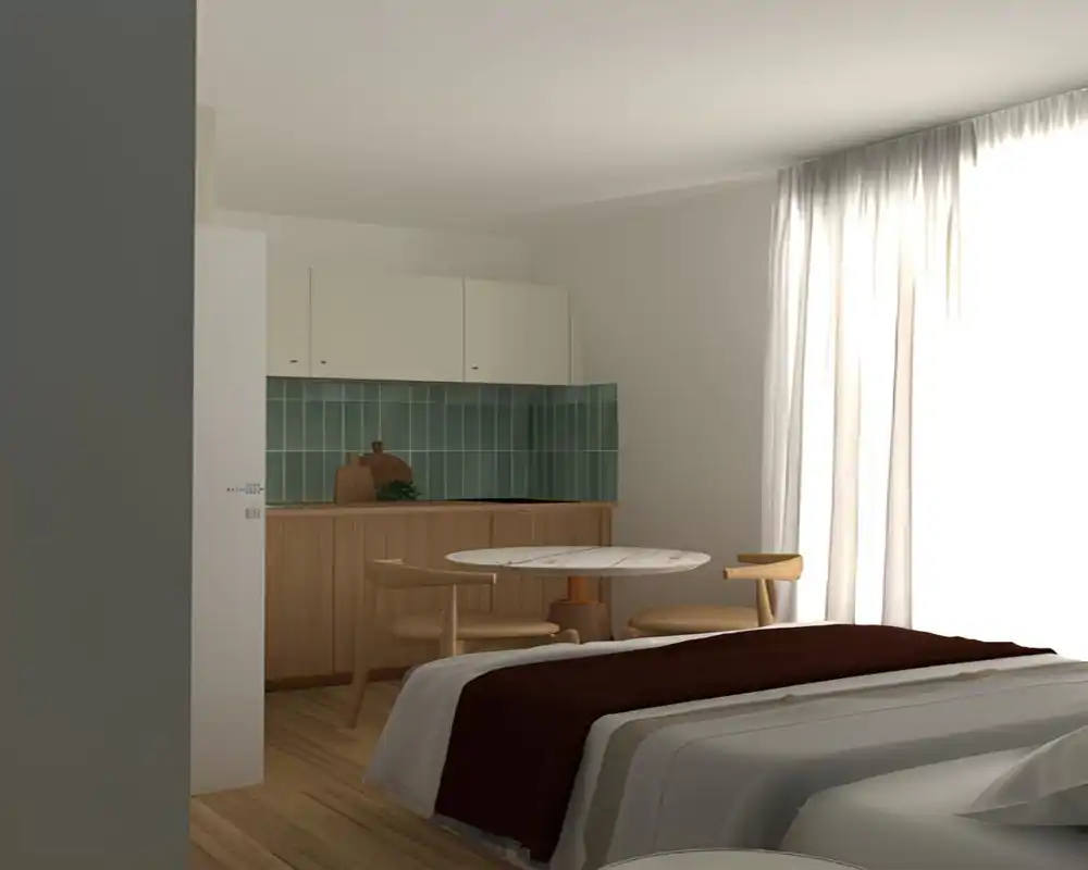 Dormitorio luminoso y minimalista con una cama cómoda en primer plano, ropa de cama en capas y una pequeña cocina con mesa redonda junto a una gran ventana que inunda el espacio de luz natural.