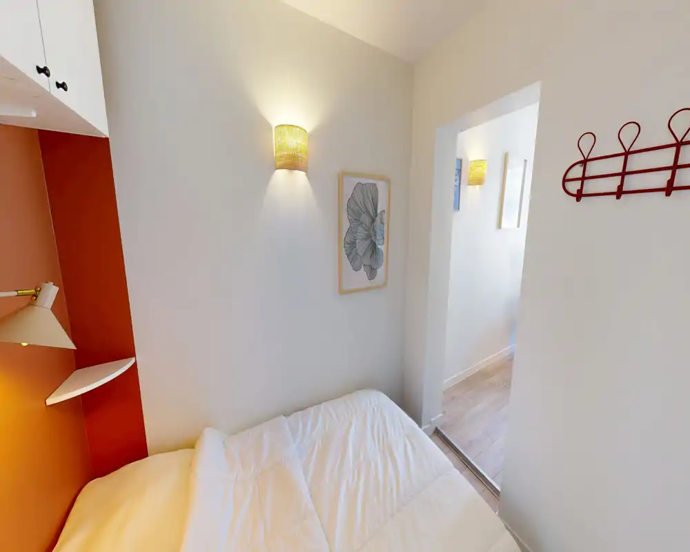 Chambre compacte et lumineuse avec lit bien fait, appliques murales chaleureuses et décoration sobre. L'espace est cosy et fonctionnel, adapté pour une personne ou un couple.