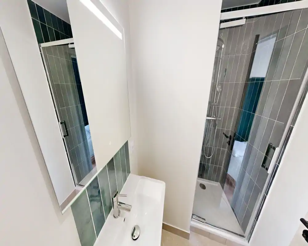 Salle de bains moderne avec lavabo mural, armoire-miroir et cabine de douche carrelée avec porte en verre ; espace lumineux, propre et compact.