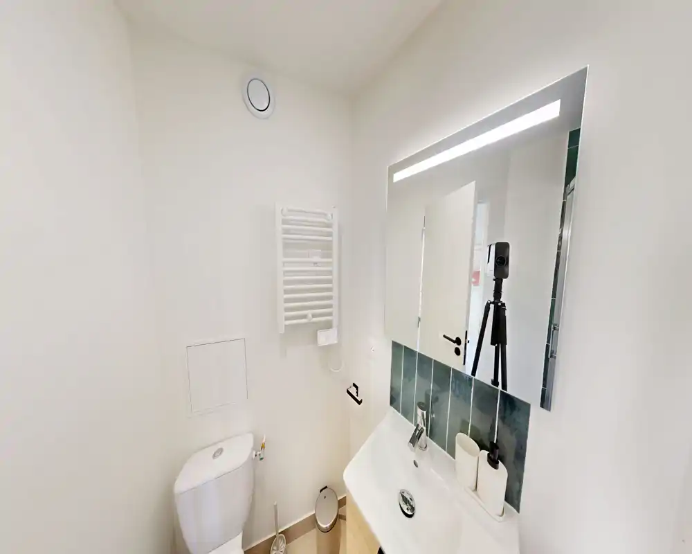 Salle de bains compacte et moderne avec WC, lavabo, miroir éclairé et sèche-serviettes ; murs blancs lumineux et finitions propres.