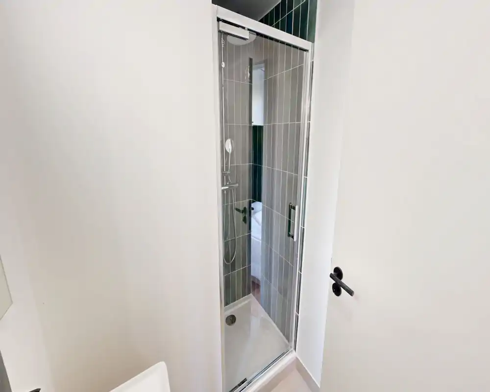 Petite salle de bains moderne avec cabine de douche à porte vitrée, carrelage gris vertical et murs blancs lumineux; équipement propre et fonctionnel.