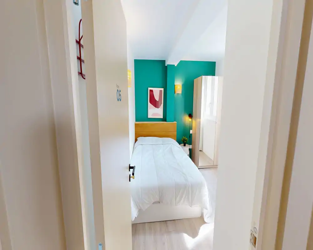 Chambre lumineuse et bien aménagée avec lit blanc, mur d'accent turquoise, tête de lit en bois et armoire ; idéale pour une location courte.