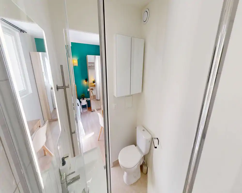 Salle de bain compacte et moderne avec WC, armoire murale et cabine de douche d'angle ; lumineuse, propre et bien éclairée.
