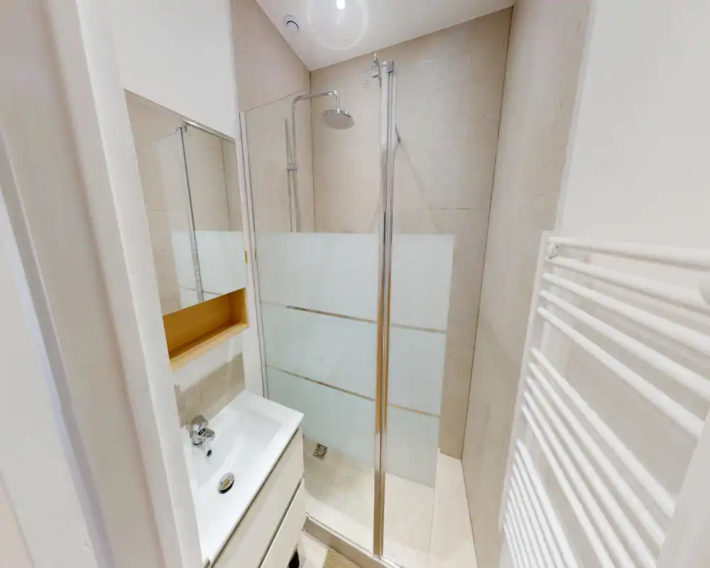 Bagno moderno compatto con doccia walk-in, parete in vetro satinato, termoarredo a parete e piccolo mobile lavabo con specchio — luminoso e pulito.