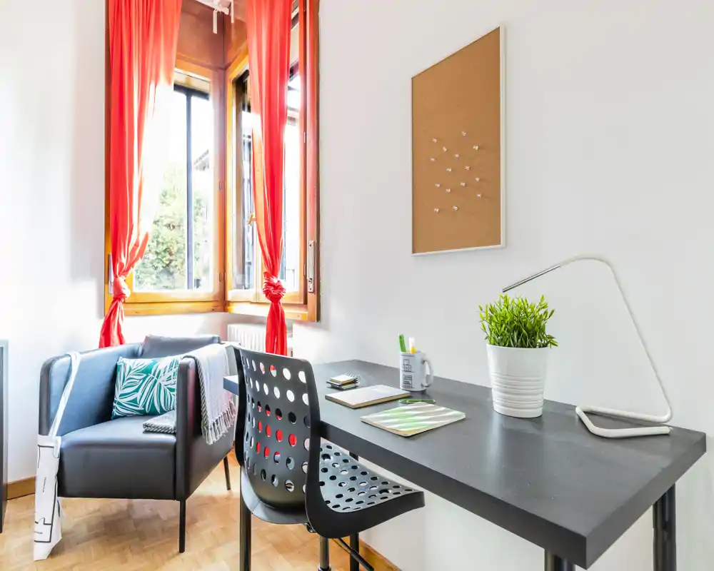 Angolo living/studio luminoso e moderno con scrivania, sedia di design e una poltrona comoda vicino alla finestra soleggiata — perfetto per lavorare da casa o rilassarsi.