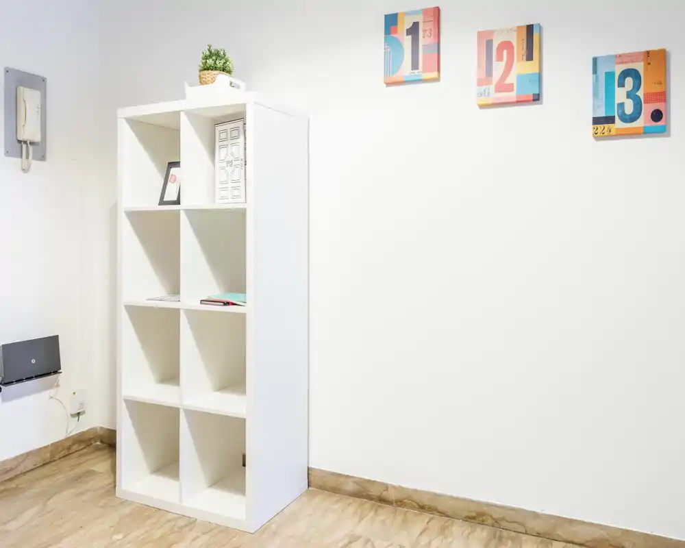 Ingresso semplice e ben illuminato o angolo di corridoio con un mobiletto bianco a cubi e decorazioni murali minimaliste — pavimento in marmo chiaro e pareti bianche pulite.
