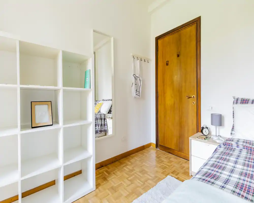 Rincón de dormitorio luminoso y bien decorado con cama individual, mesita de noche y estantería; la luz natural aporta una sensación fresca y aireada.